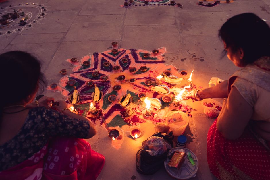 Two women create a colorful rangoli and light diyas for Diwali celebration, showcasing Indian culture and tradition.