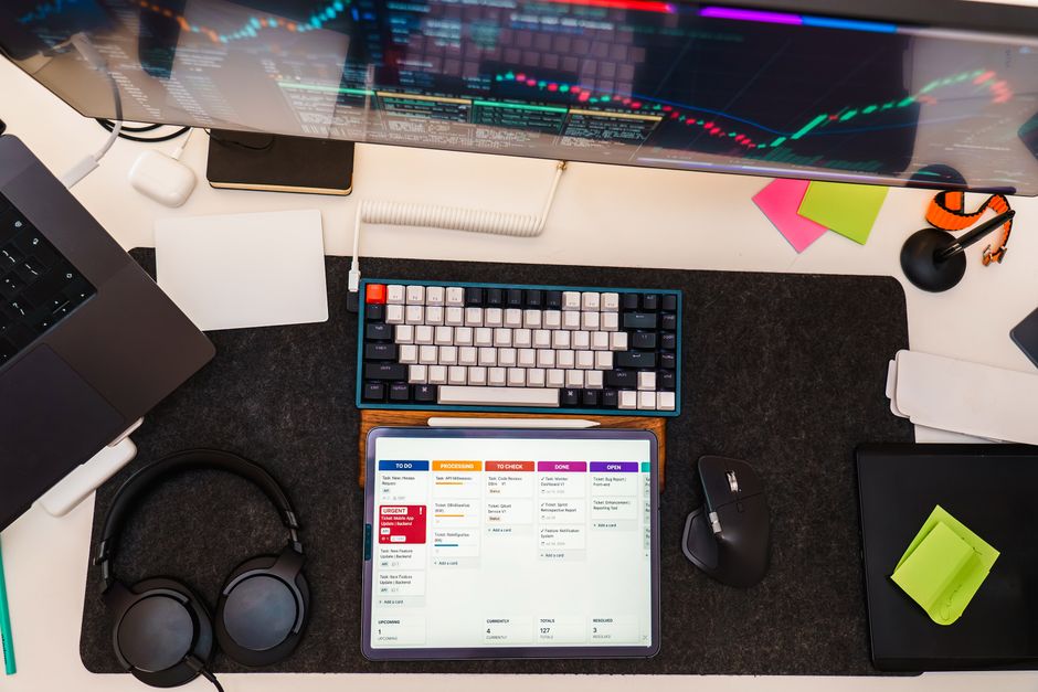 Top view of a tech workspace featuring a digital tablet, keyboard, monitor, and headphones for project management.